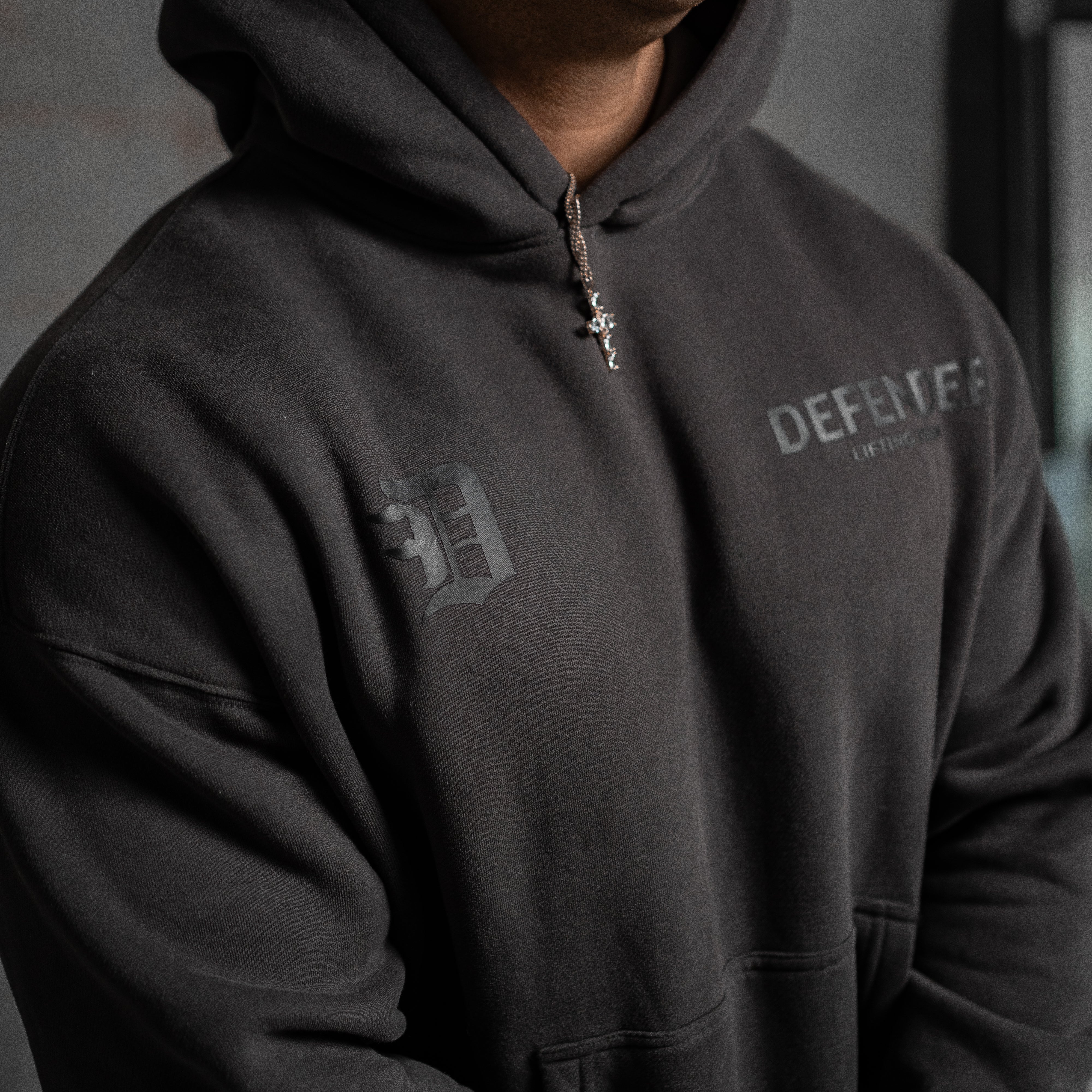 Close up shot of a person wearing a black hoodie with logos on a blurred background
