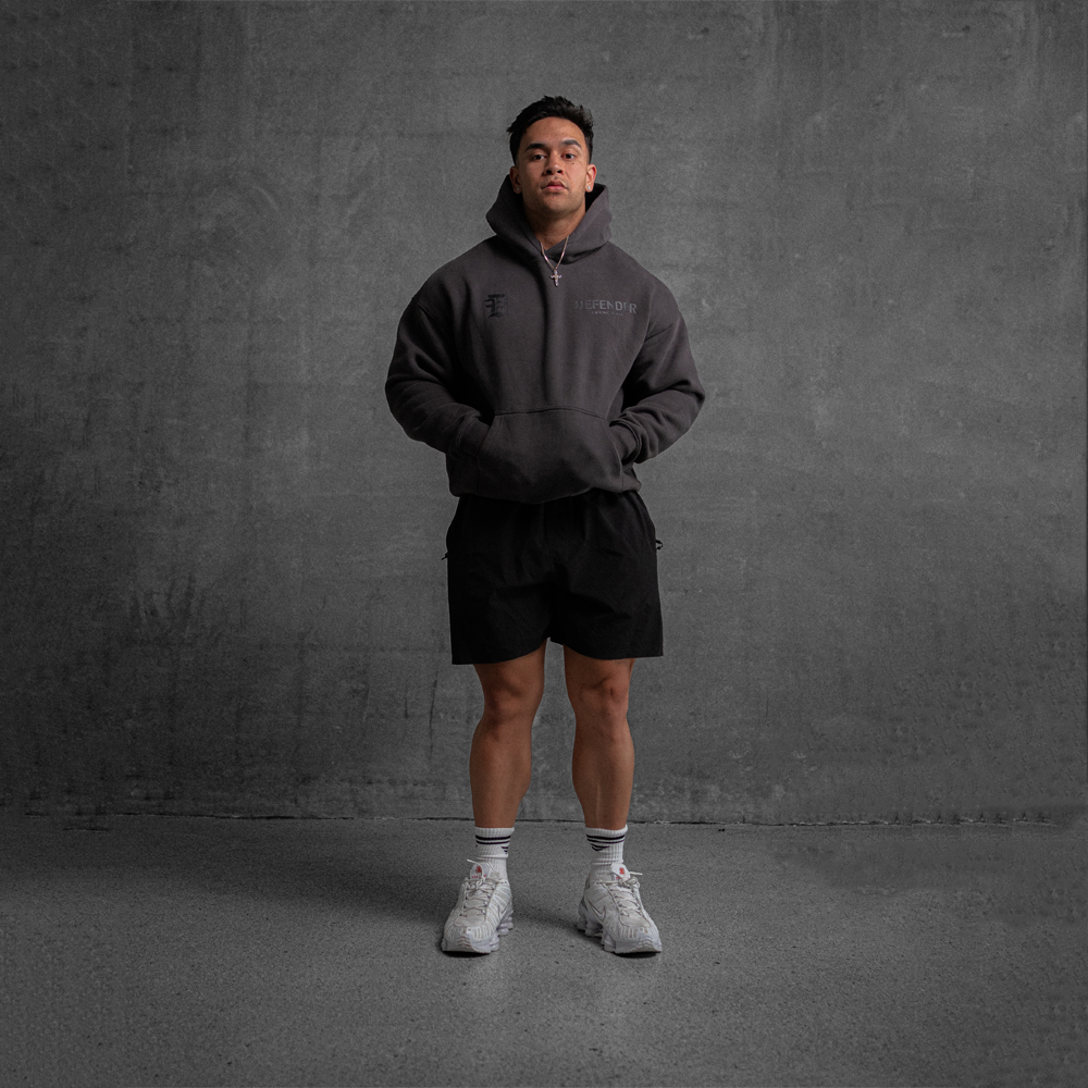 Person wearing a dark hoodie and shorts with white sneakers against a gray background