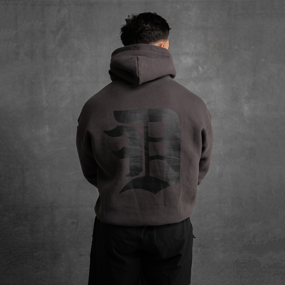 Person wearing a dark hoodie with a logo on the back against a gray background