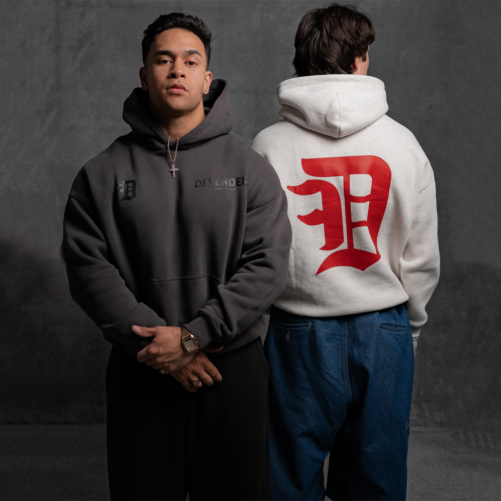 Two people wearing hoodies, one gray with 'DEFENDERS' text, the other white with a red logo on the back.